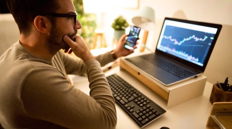 an-investor-looking-at-a-chart-on-their-computer-screen-while-holding-a-smartphone.jpg