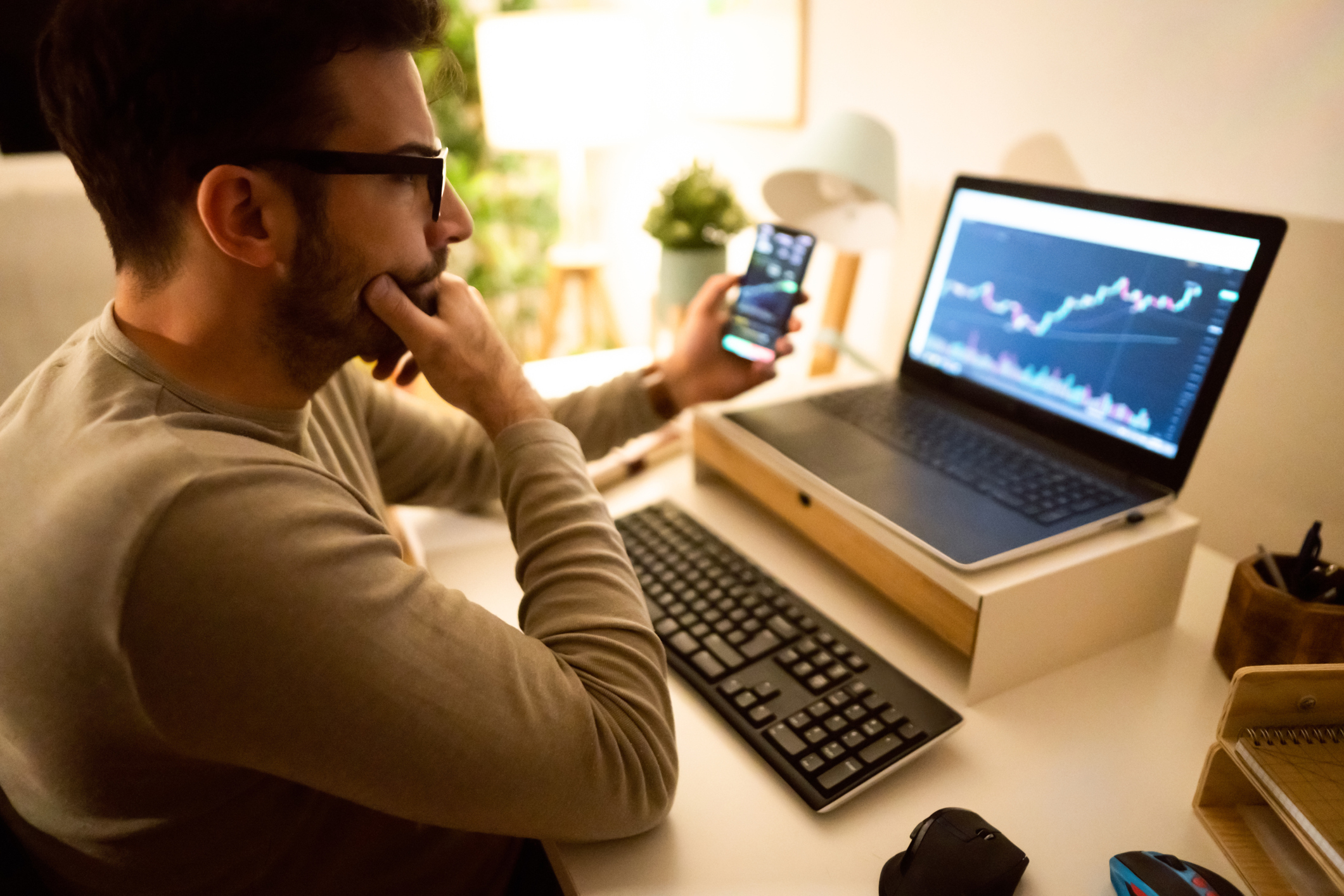 an investor looking at a chart on their computer screen while holding a smartphone
